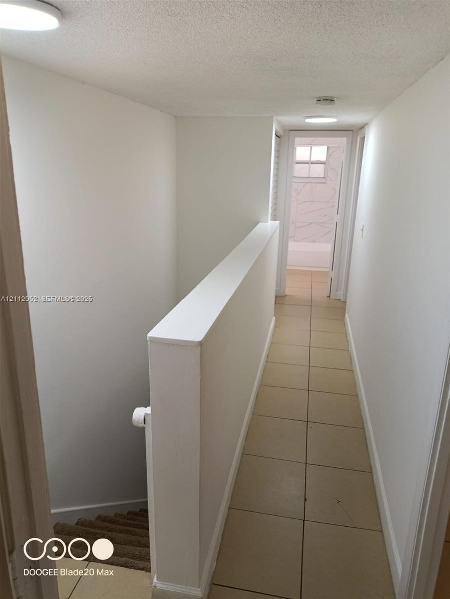 Hallway featuring neutral large-format tile flooring, flush-mount ceiling lighting, and a painted half-wall staircase partition