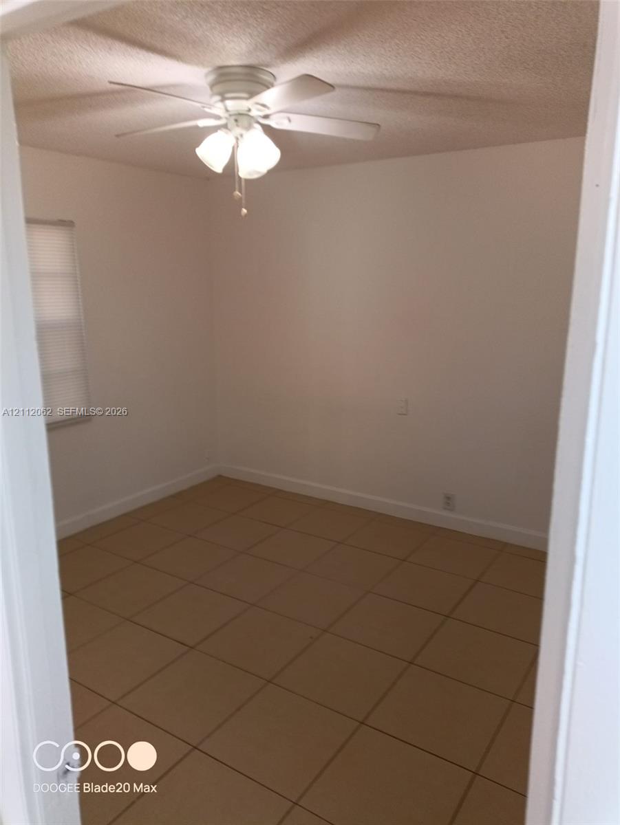 Square ceramic tile flooring, neutral wall finish, and a ceiling-mounted fan with integrated lighting