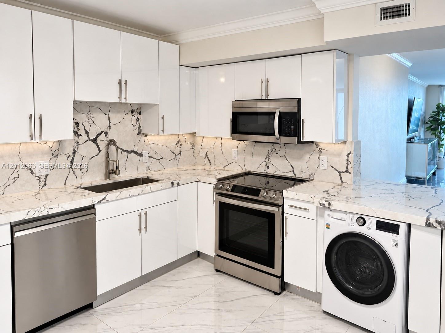 Kitchen featuring high-gloss white cabinetry, veined stone-finish countertops and backsplash, stainless steel appliances, and large-format tile flooring Kitchen featuring high-gloss white cabinetry, veined stone-finish countertops and backsplash, stainless steel appliances, and large-format tile flooring