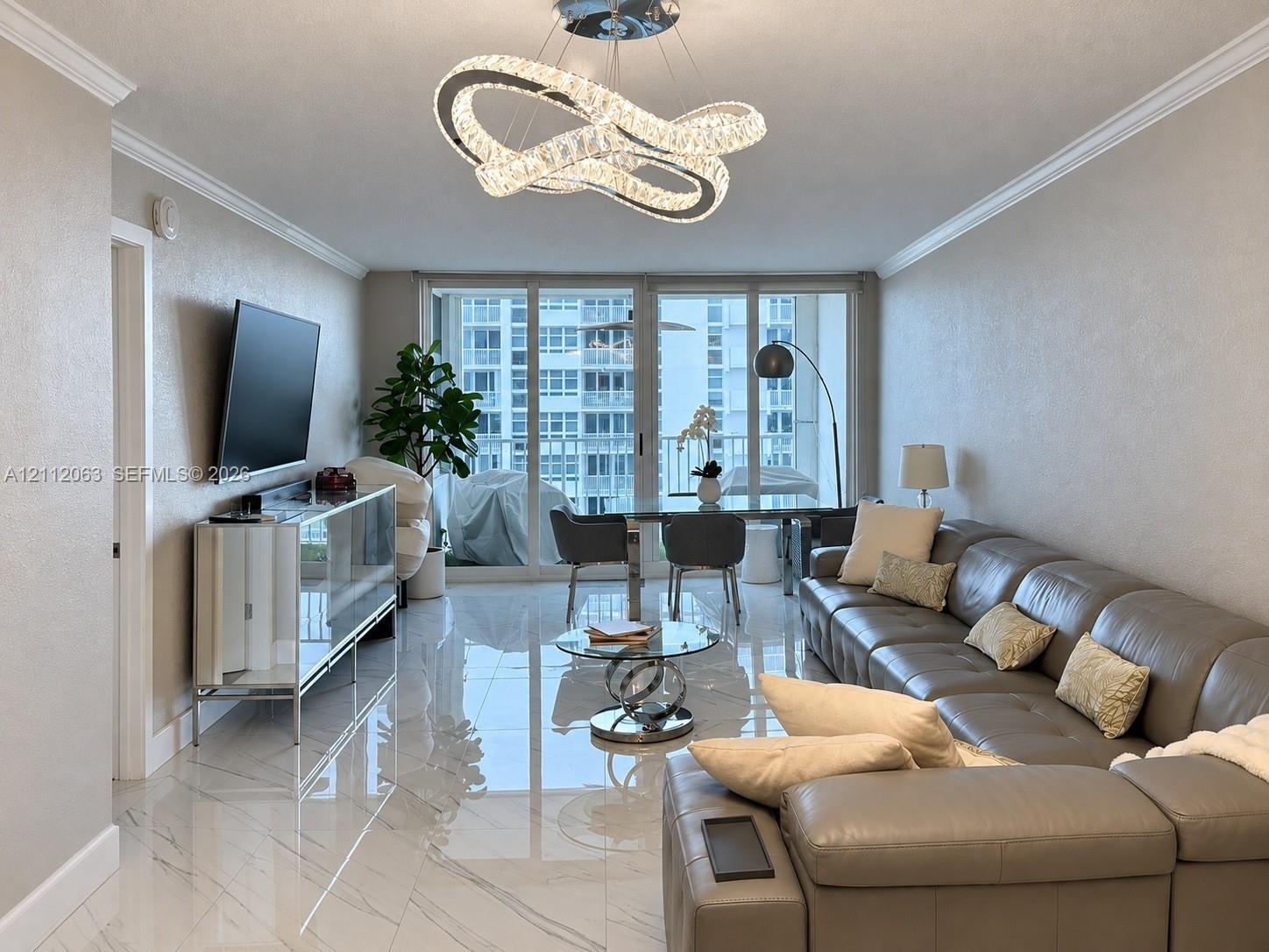 Polished tile flooring with subtle veining, contemporary geometric crystal chandelier, and floor-to-ceiling glass sliding doors opening to a private balcony Polished tile flooring with subtle veining, contemporary geometric crystal chandelier, and floor-to-ceiling glass sliding doors opening to a private balcony