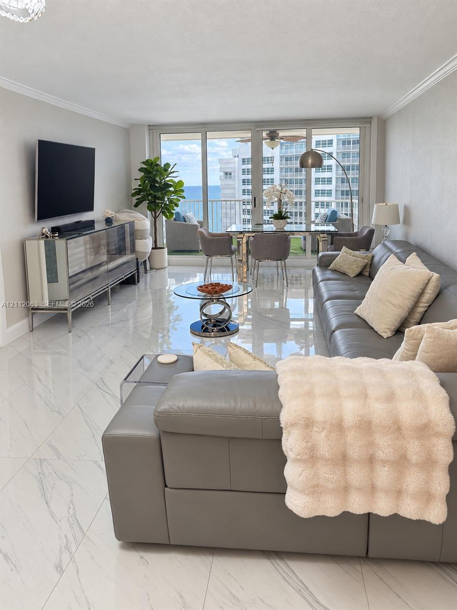 Open-concept living space featuring high-gloss large-format floor tiling, crown molding, floor-to-ceiling glass sliding doors, and a private balcony Open-concept living space featuring high-gloss large-format floor tiling, crown molding, floor-to-ceiling glass sliding doors, and a private balcony