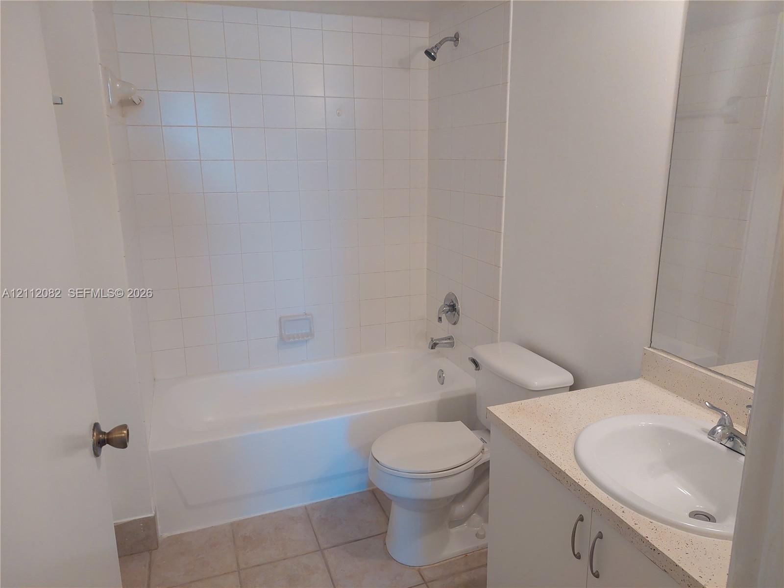 Bathroom featuring a white vanity with a solid-surface countertop, an integrated sink, floor-to-ceiling ceramic wall tile surrounding the bathtub, and neutral tile flooring