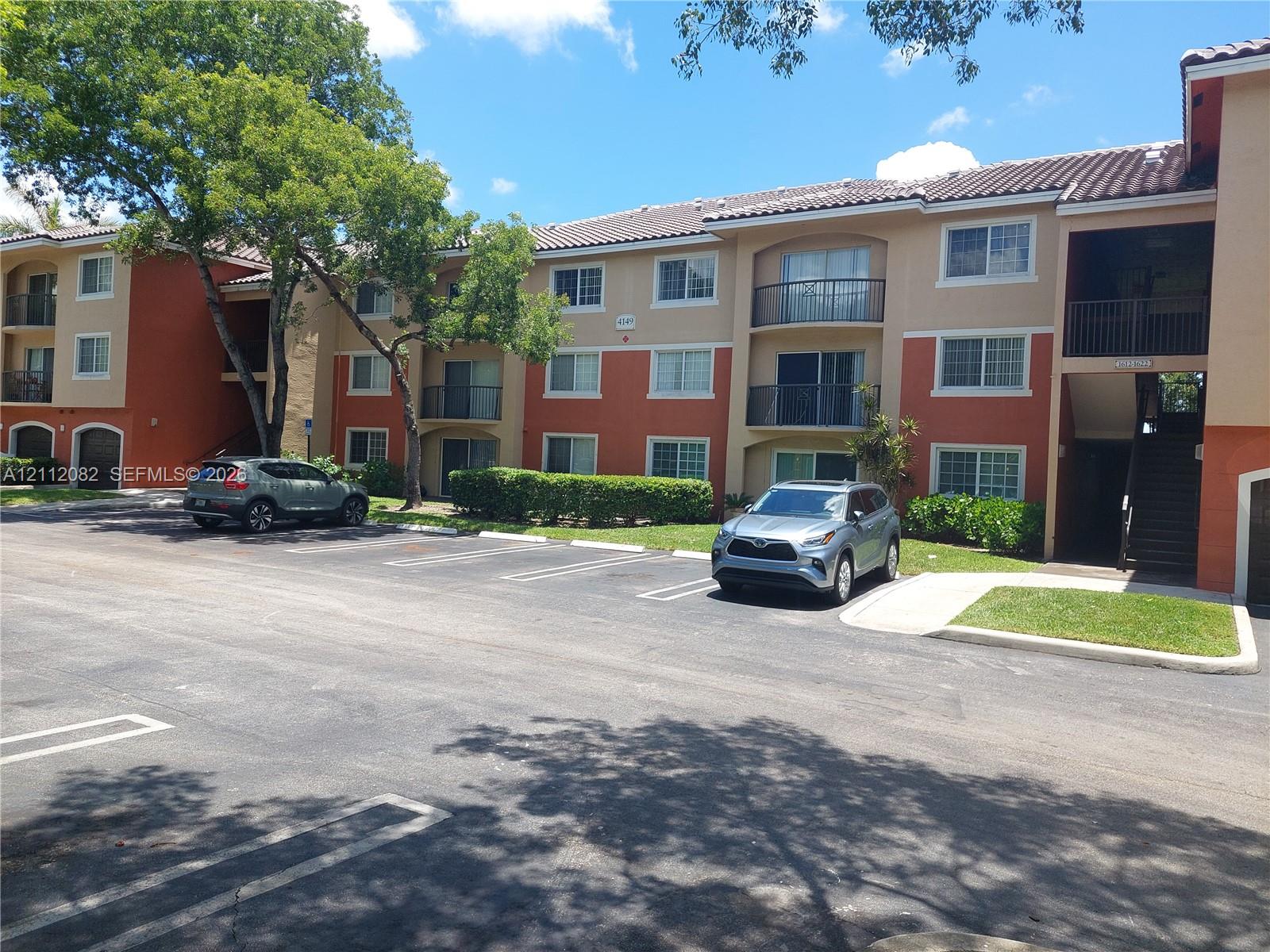 Multi-story building exterior featuring a tiled roof, stucco facade, private balconies with railings, and designated surface parking