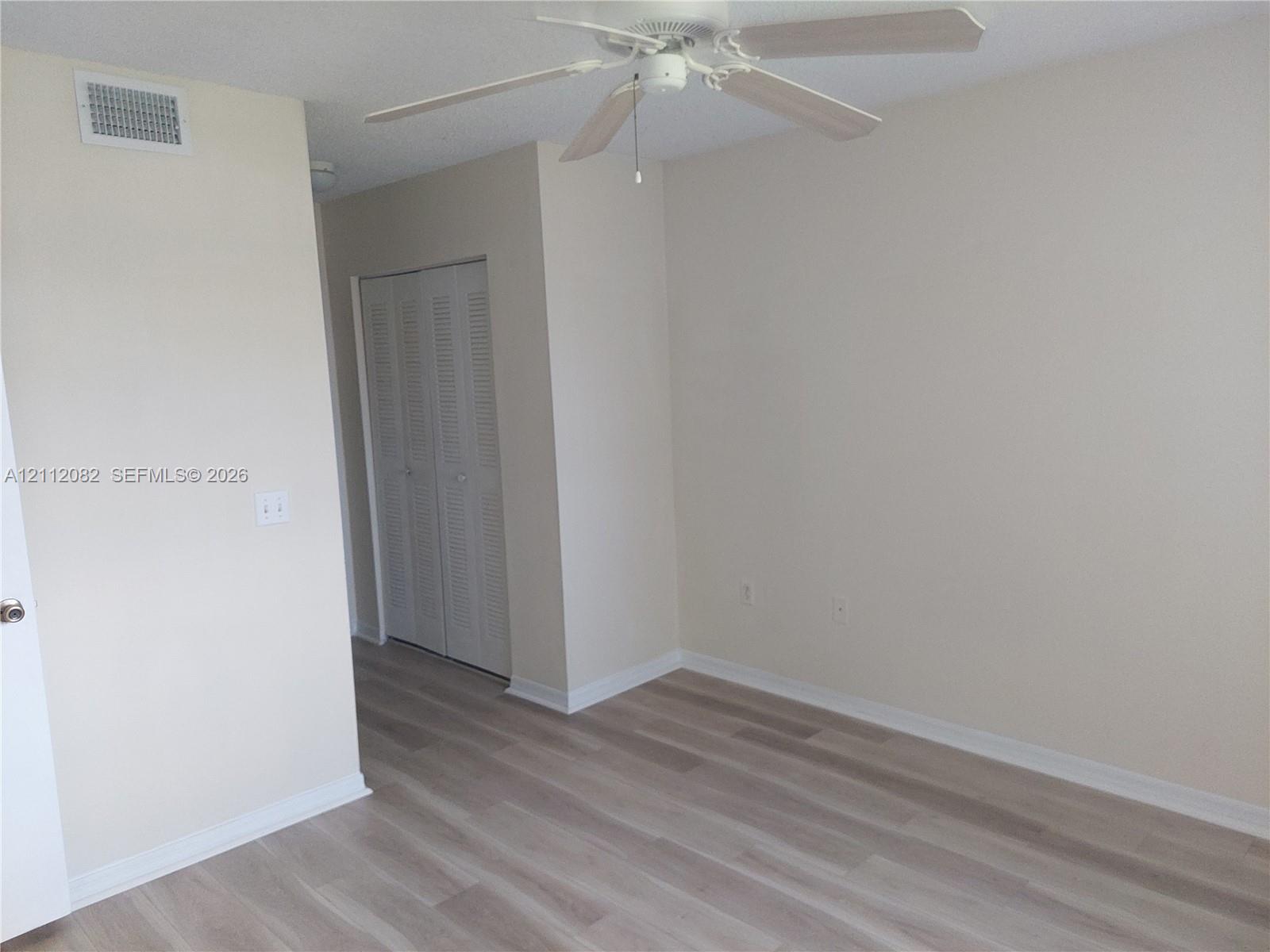 Neutral-toned interior featuring wood-finish flooring, a ceiling fan with light fixture, and louvered closet doors