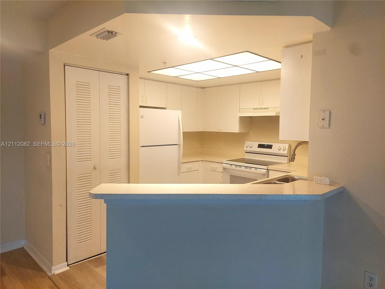 Kitchen featuring white cabinetry, solid-surface countertops, breakfast bar, recessed paneling, and integrated fluorescent lighting
