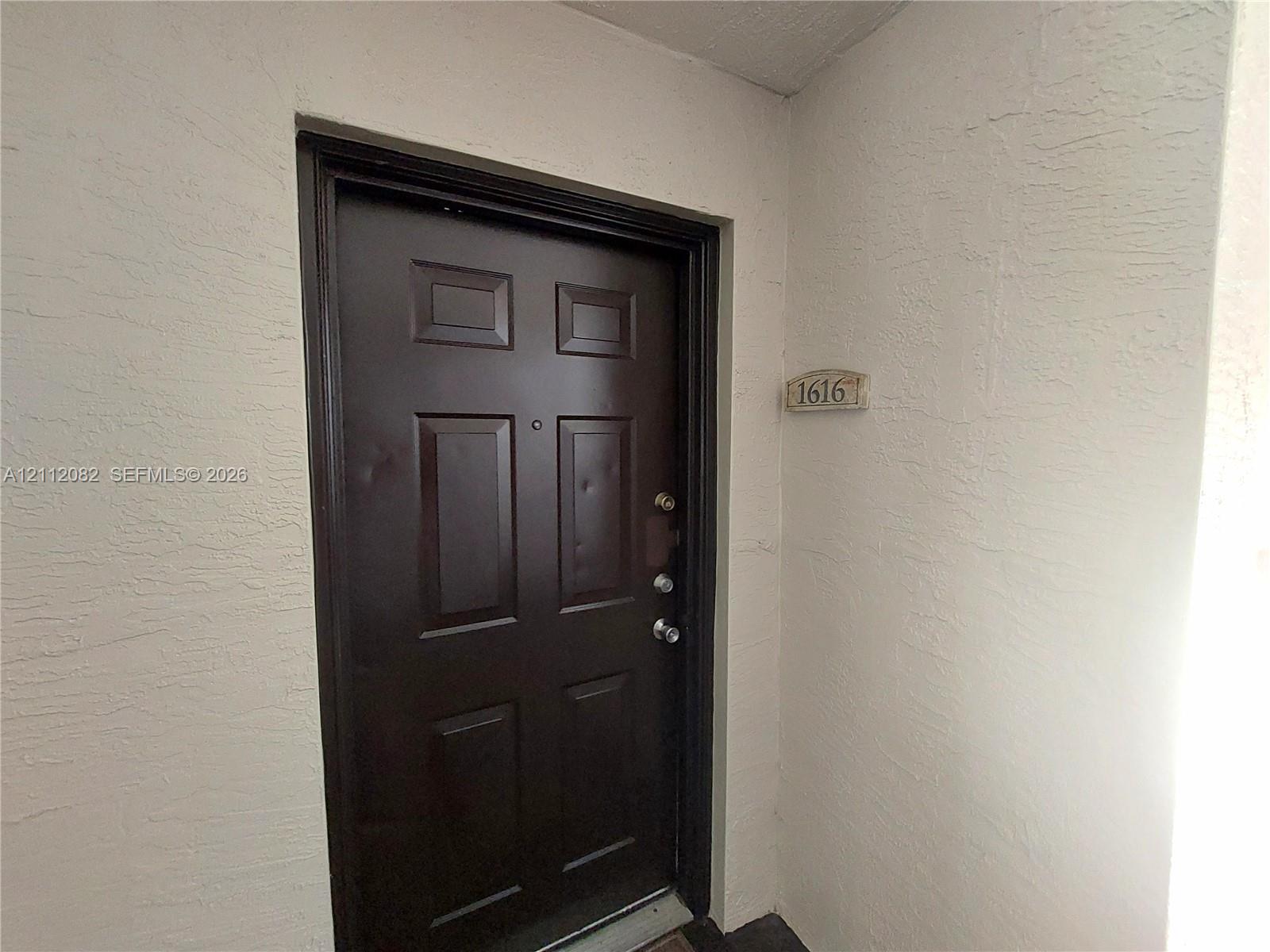Solid-core, six-panel dark finish entry door featuring a metal peep hole, deadbolt, and door handle hardware