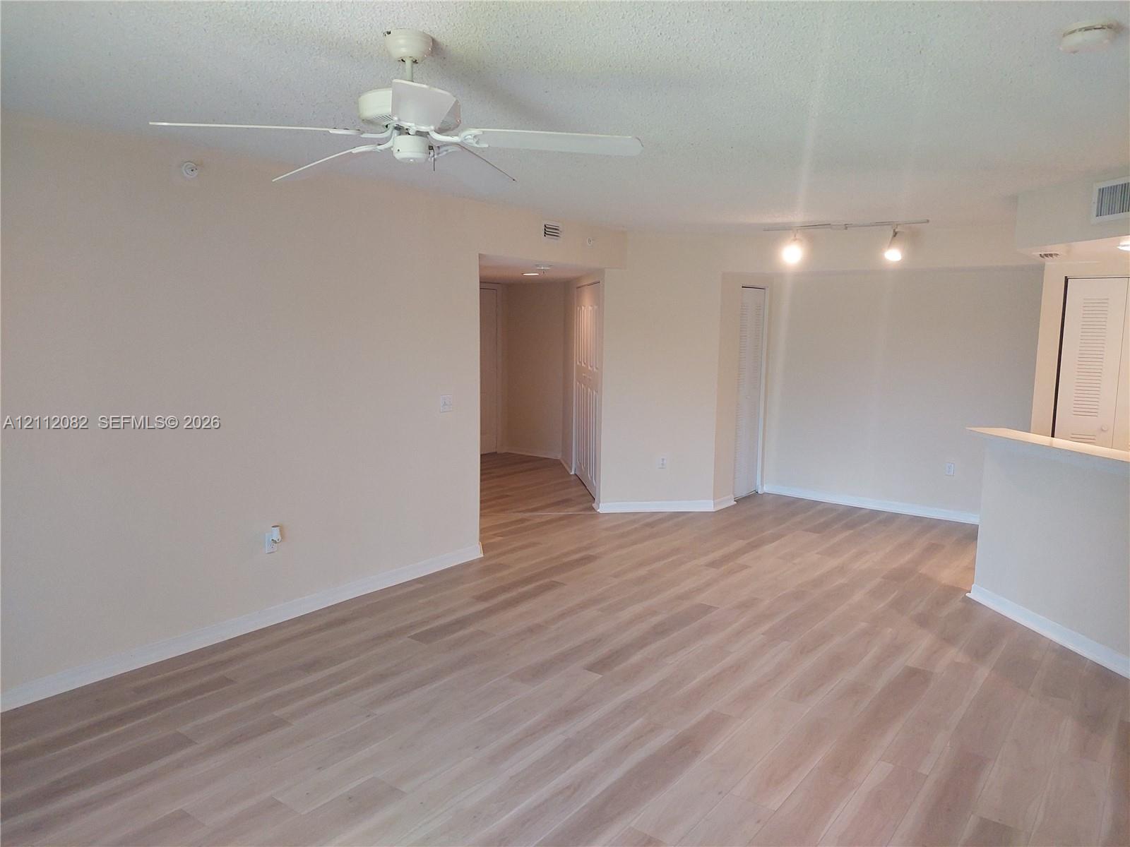 Neutral-toned living space featuring light-tone wood-finish flooring, a white ceiling fan, and adjustable track lighting