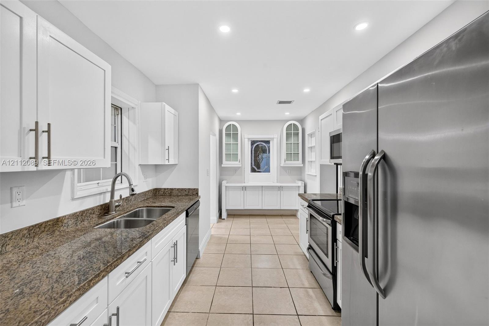 Kitchen featuring white cabinetry, stone countertops, double-basin stainless steel sink, recessed lighting, and tile flooring
