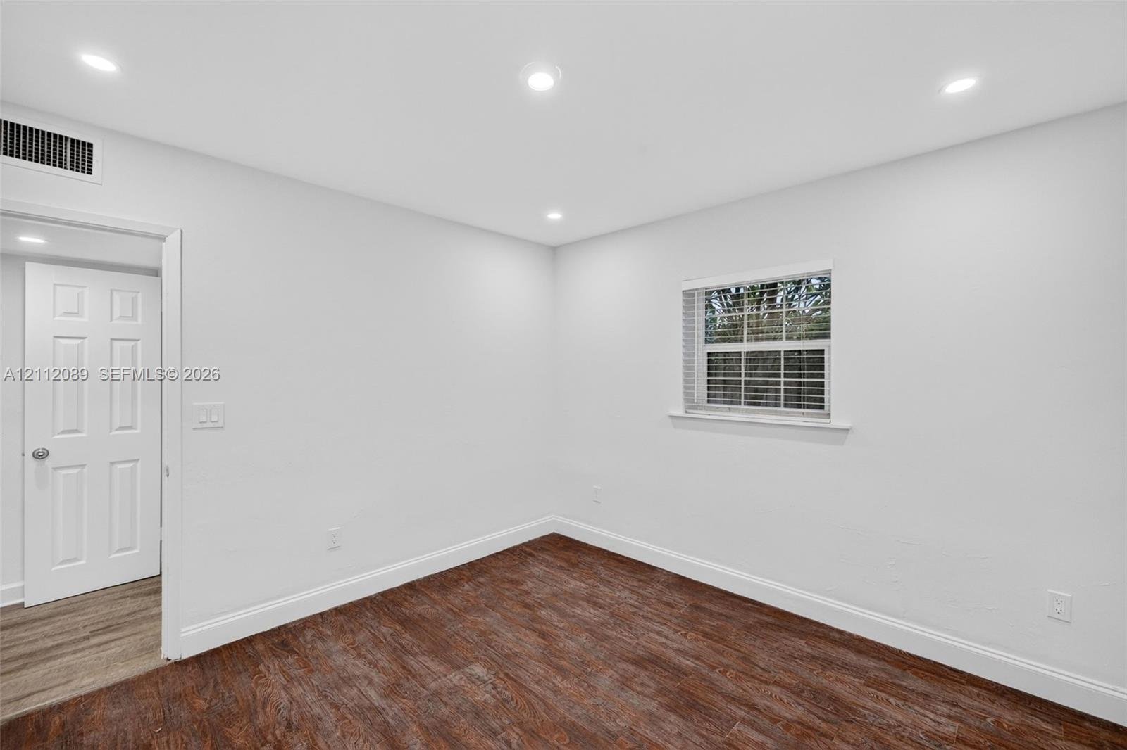 Neutral interior space featuring wood-finish flooring, recessed lighting, a multi-pane window with blinds, and a six-panel door