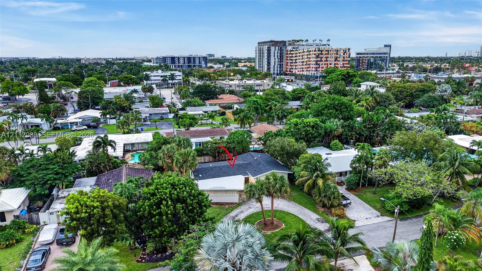 Aerial perspective of a residential property featuring a dark-toned shingled roof, a curved driveway, and established palm trees within a landscaped lot