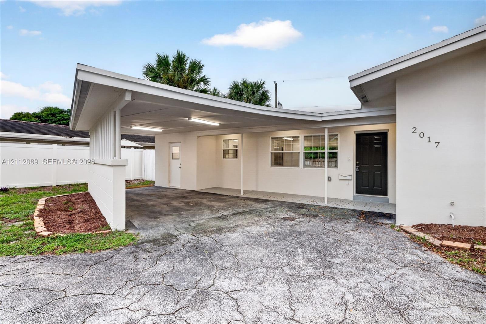 Exterior featuring a covered carport, recessed lighting, solid entry door, and perimeter vinyl fencing