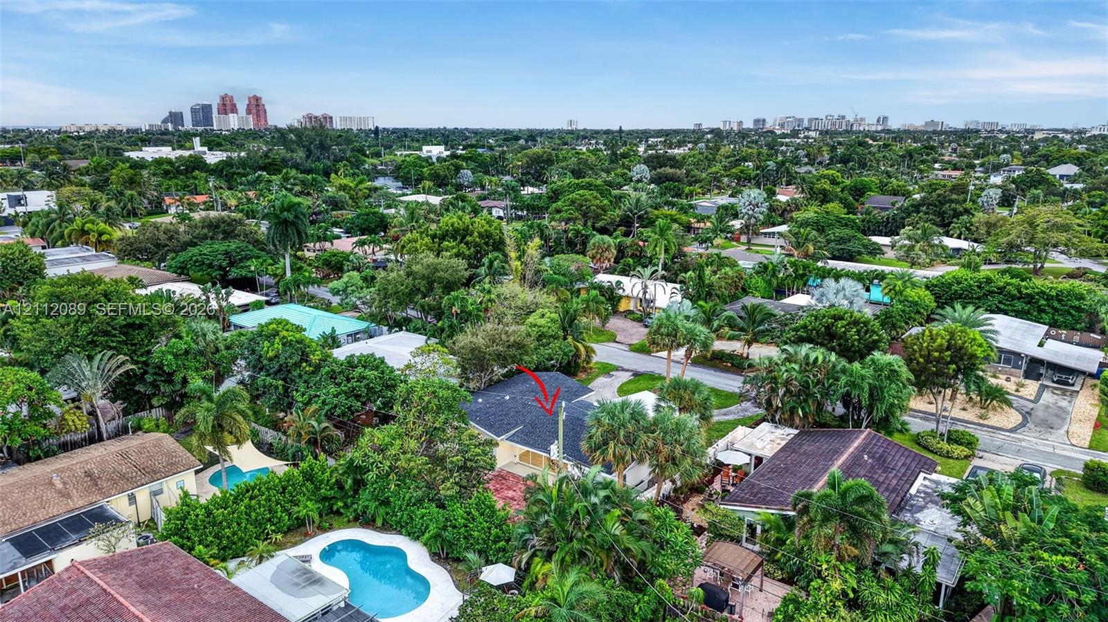 Aerial perspective of property featuring a shingled roof, mature tropical landscaping, and a surrounding neighborhood canopy