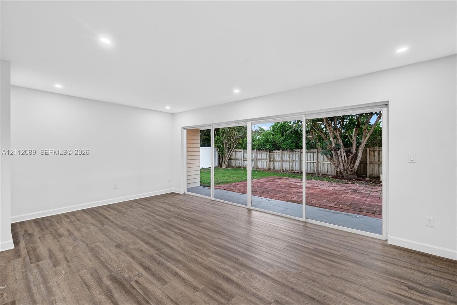 Interior space featuring wood-finish flooring, recessed lighting, and expansive multi-panel sliding glass doors opening to a paved patio and fenced yard
