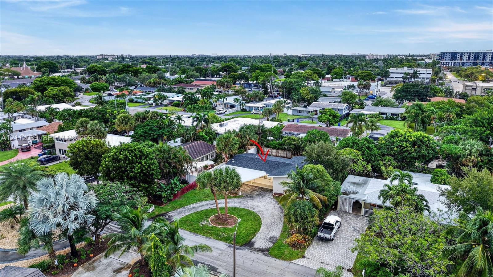Aerial perspective featuring a shingled roof, circular driveway, mature landscaping, and an expansive lot