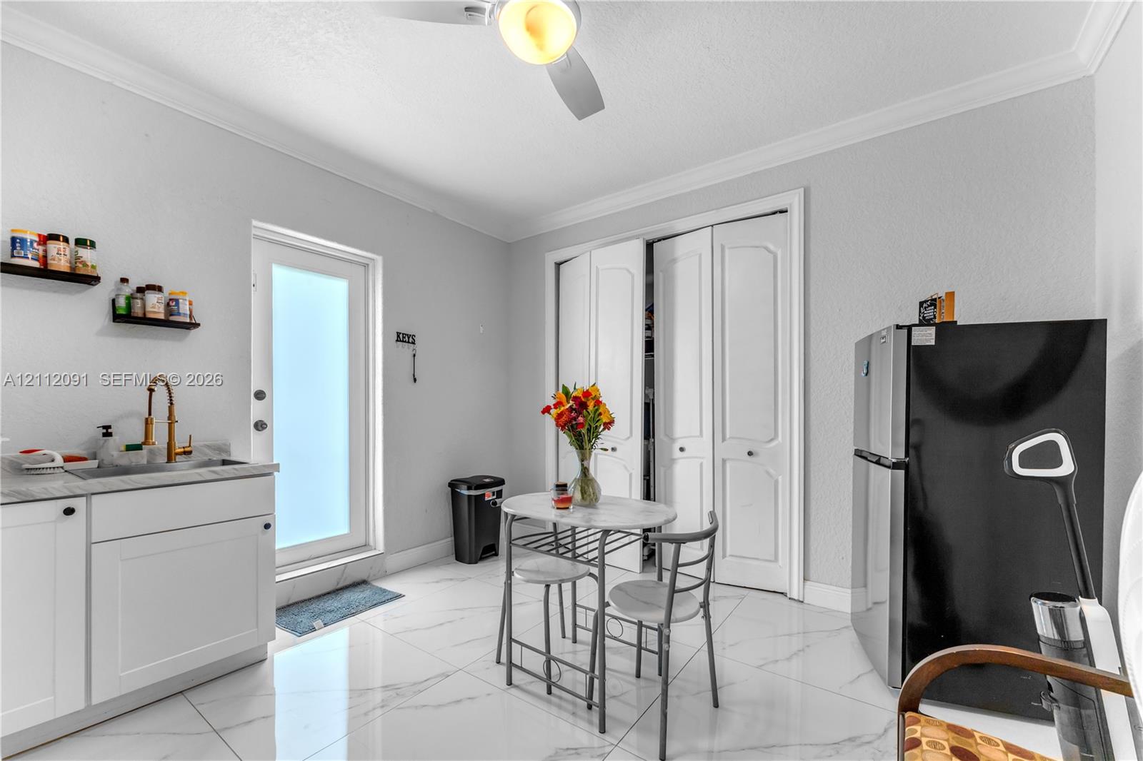 Polished tile flooring, built-in lower cabinetry with stone-finish countertops, undermount sink with brass-finish faucet, bi-fold closet doors, and exterior door with frosted glass insert