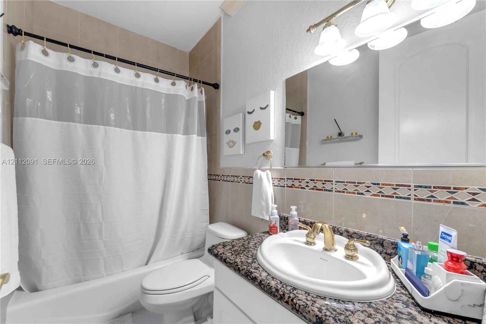Bathroom featuring a stone-surface vanity countertop, drop-in sink with brass-toned hardware, decorative tile backsplash, and a tub-shower combination with full-height tile wall surround