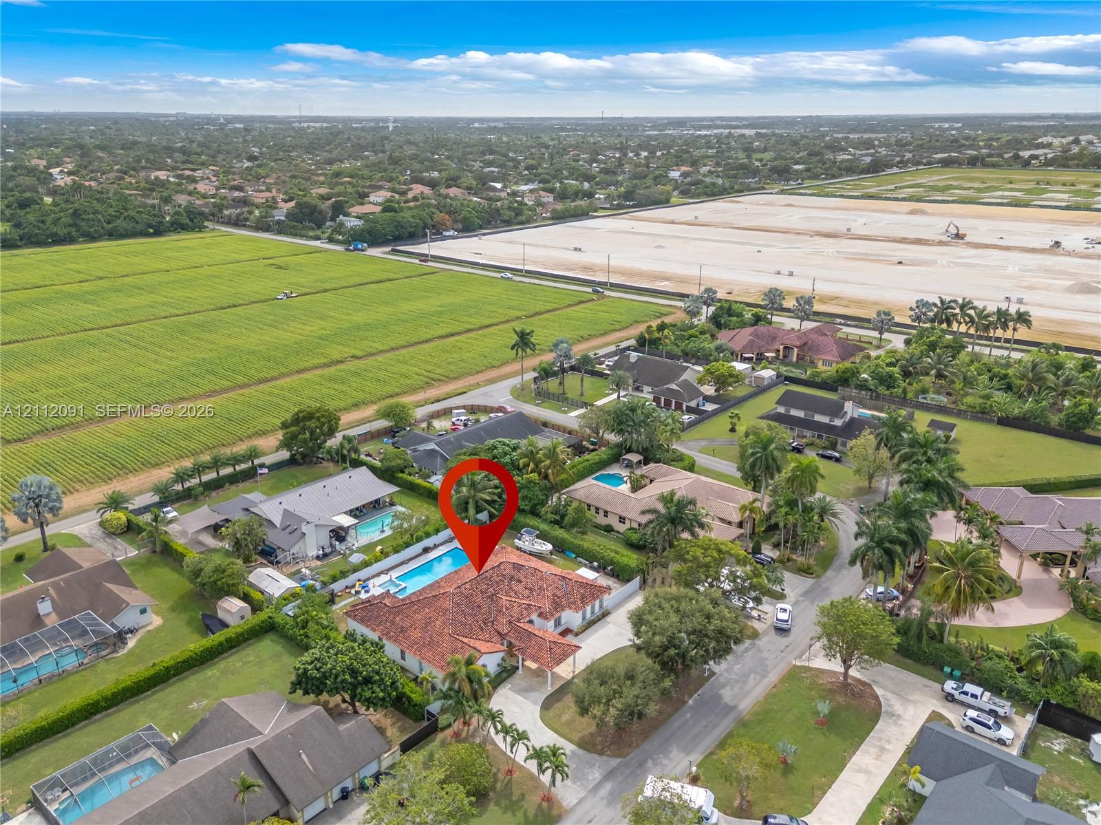Aerial perspective of a property featuring a multi-hipped tile roof, an expansive paved driveway, and a private rear swimming pool