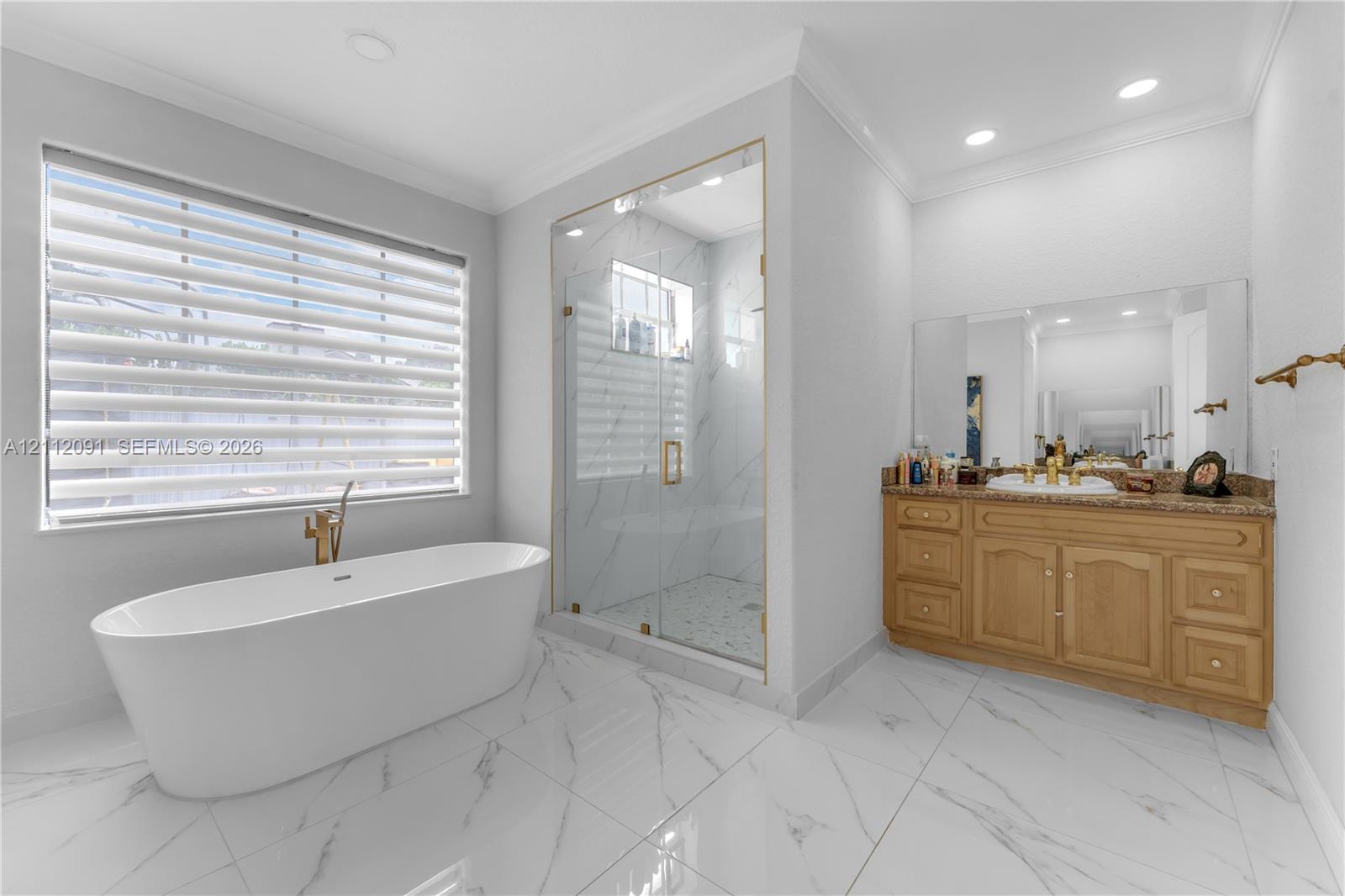 Freestanding soaking tub with gold-tone fixtures, walk-in glass-enclosed shower with tiled surround, stone-finish vanity countertop, and polished tile flooring