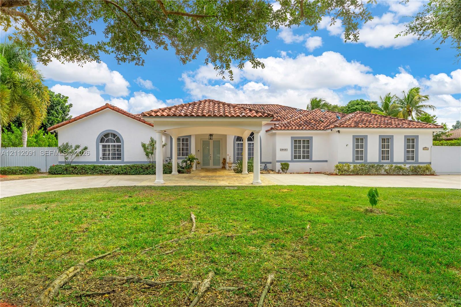Stucco exterior featuring a covered porte-cochre, red tile roofing, arched windows, and a paved circular driveway