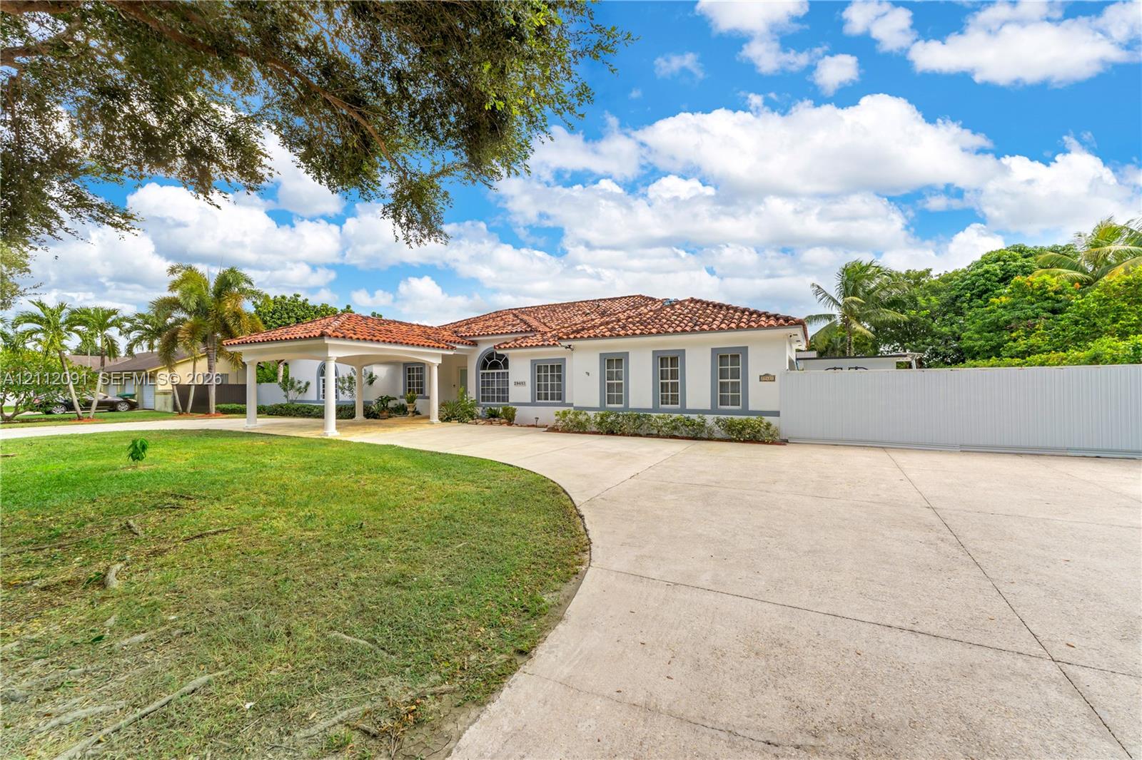 Single-story residence featuring a clay tile roof, covered porte-cochre, multi-pane windows, expansive concrete motor court, and perimeter privacy fencing