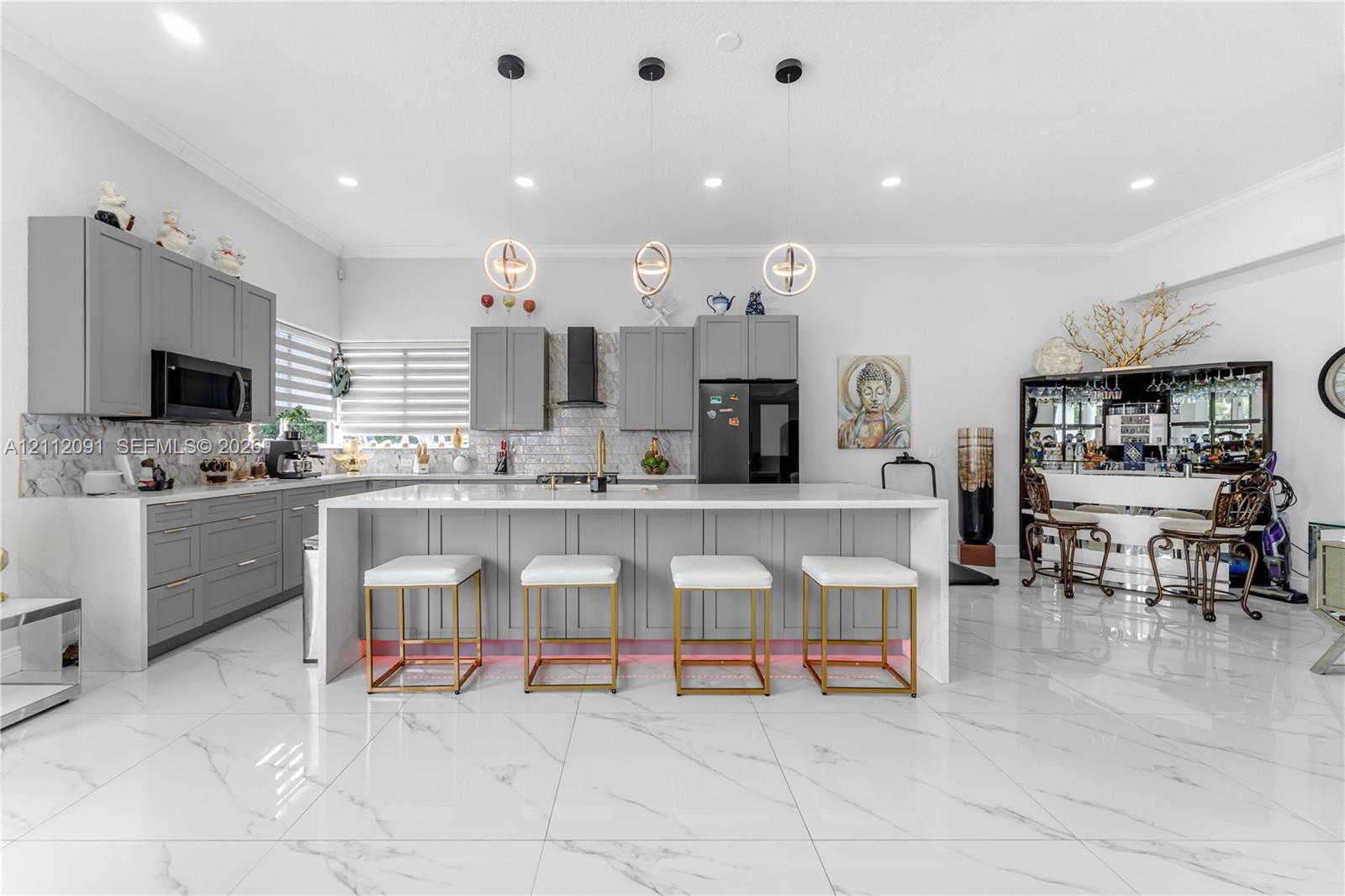 Kitchen featuring light-gray shaker-style cabinetry, quartz countertops, a stone-tile backsplash, polished large-format tile flooring, and three contemporary spherical pendant lights suspended over a central island