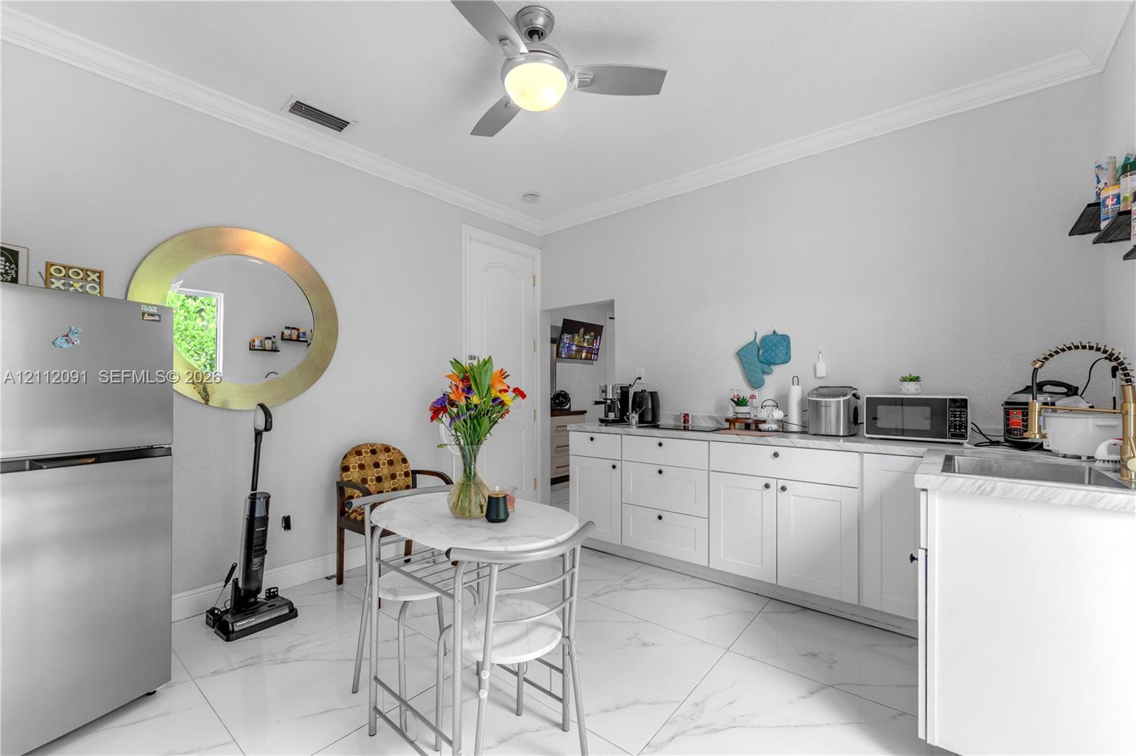 Kitchen featuring white shaker-style cabinetry, solid-surface countertops, large-format tile flooring, a stainless steel refrigerator, and a ceiling-mounted light fixture