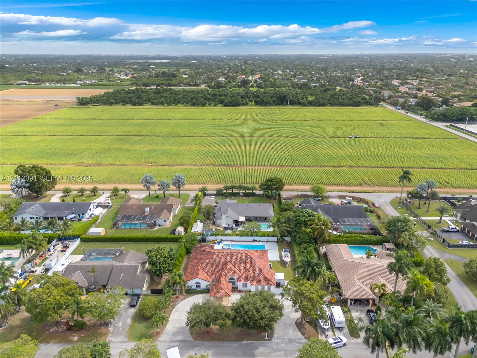 Aerial perspective featuring a property with a clay tile roof, paved circular driveway, private swimming pool, and expansive green space backdrop