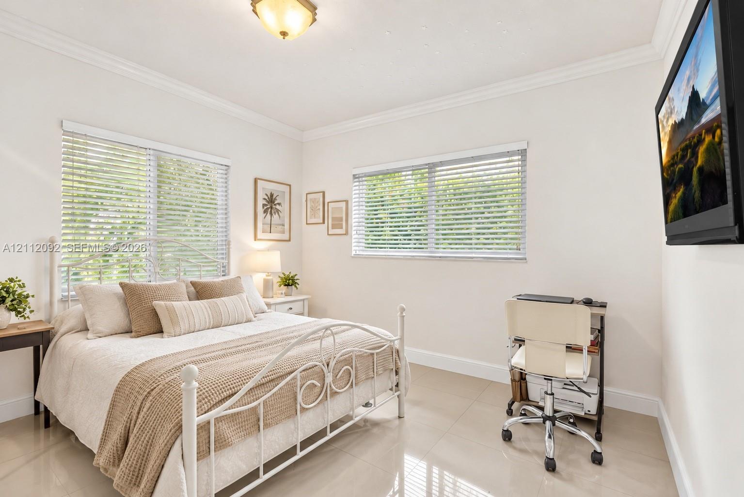 Neutral-toned tile flooring, crown molding, and dual windows equipped with horizontal blinds
