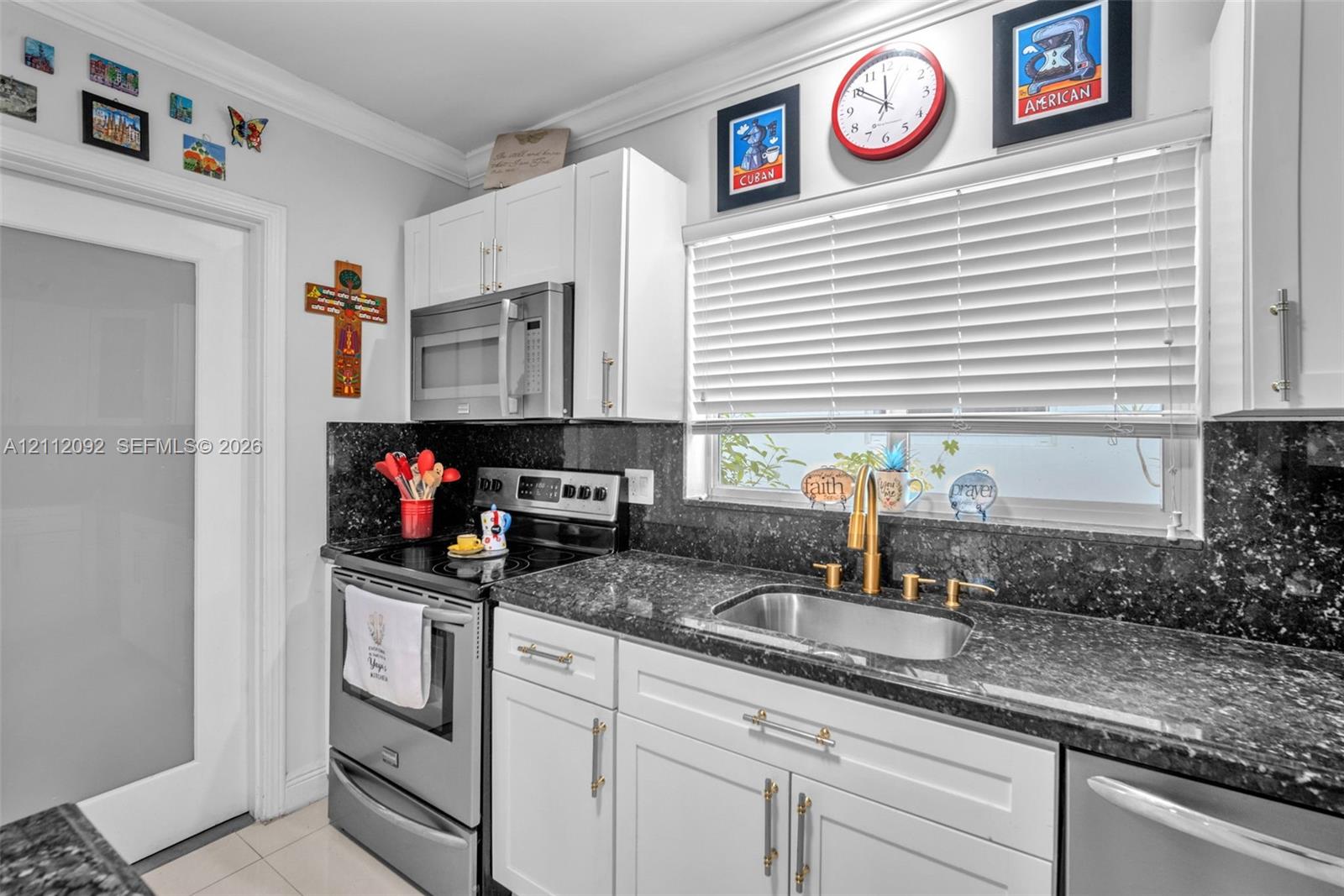 Kitchen featuring white shaker-style cabinetry, dark stone countertops, stainless steel appliances, a brass-toned gooseneck faucet, and a frosted glass panel door