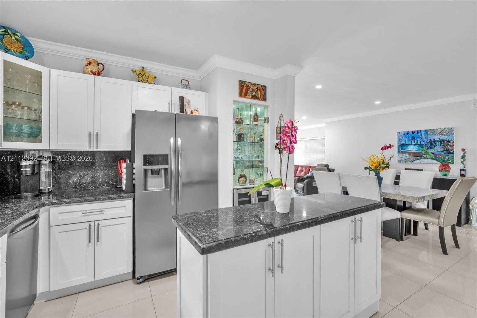 Kitchen featuring white shaker-style cabinetry, dark stone countertops, a central island, recessed lighting, and a built-in glass-front display cabinet
