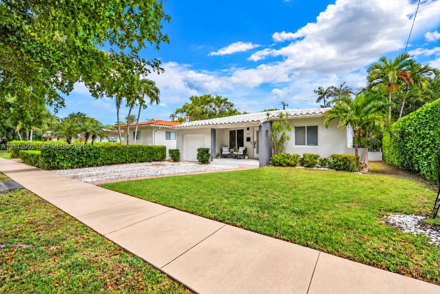 Single-story residence featuring a barrel tile roof, white stucco exterior, attached garage, stone-surfaced driveway, and landscaped shrubbery Single-story residence featuring a barrel tile roof, white stucco exterior, attached garage, stone-surfaced driveway, and landscaped shrubbery