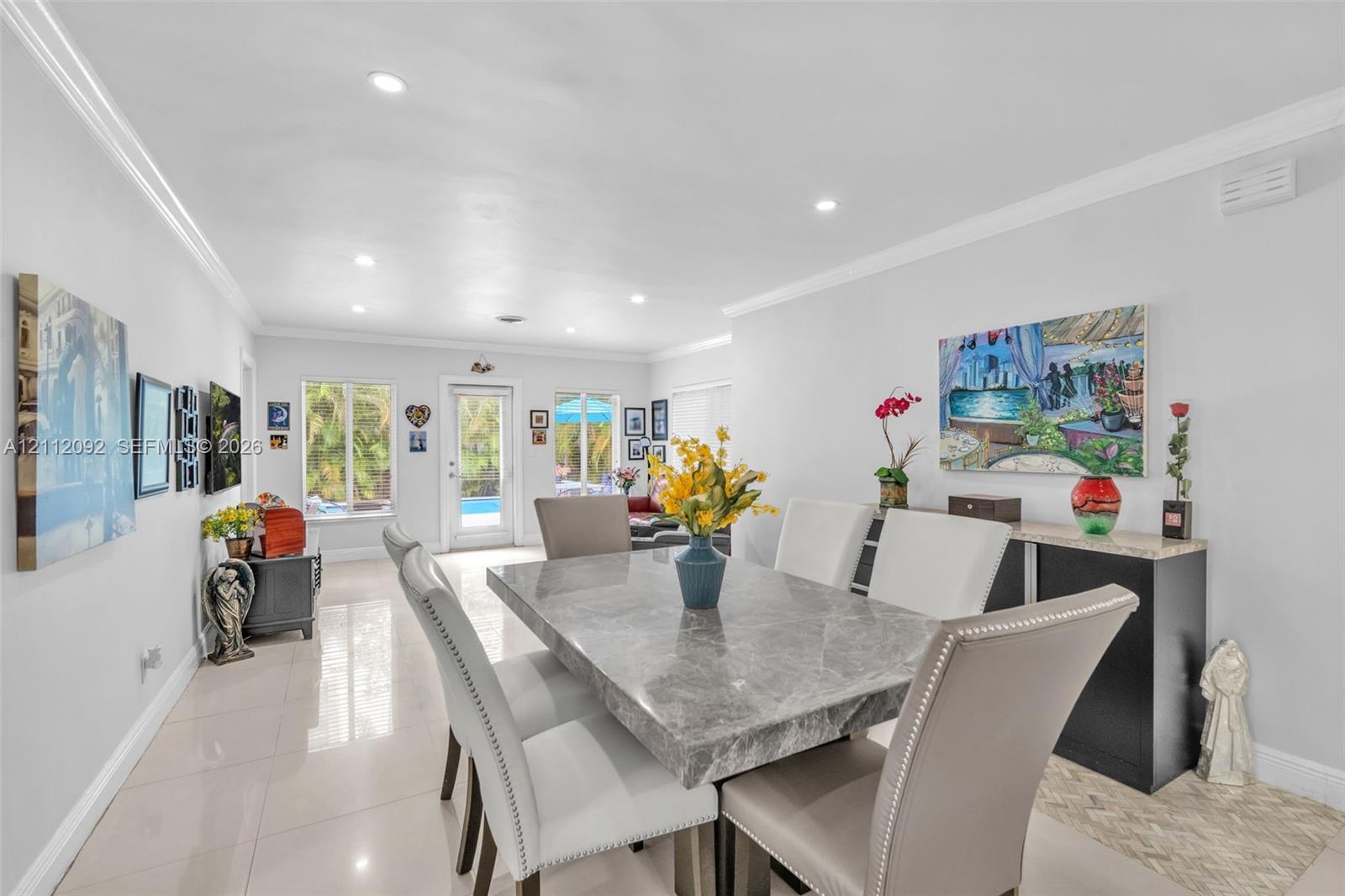 Open-concept interior featuring large-format tile flooring, recessed lighting, crown molding, and a glass-paneled exterior door