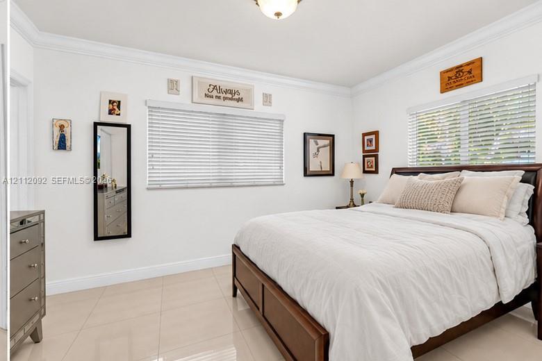 Room featuring large-format tile flooring, crown molding, and dual windows with horizontal blinds
