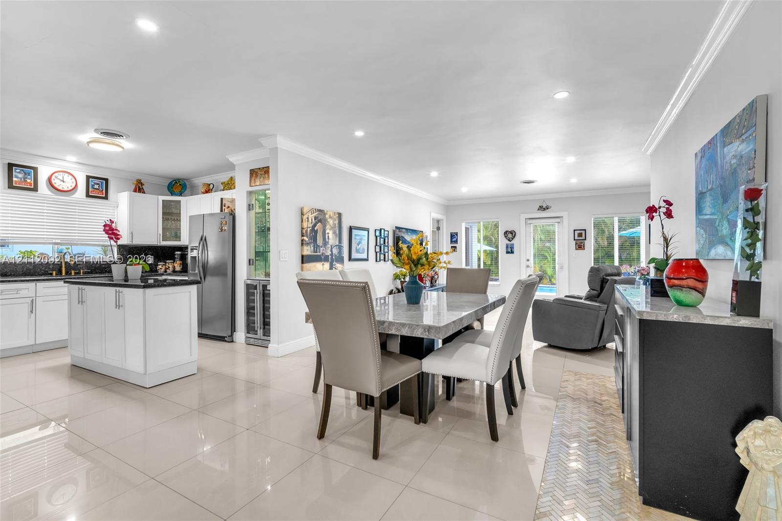 Open-concept interior featuring large-format tile flooring, recessed lighting, and a kitchen with white cabinetry, a center island with dark countertops, and a built-in wine cooler