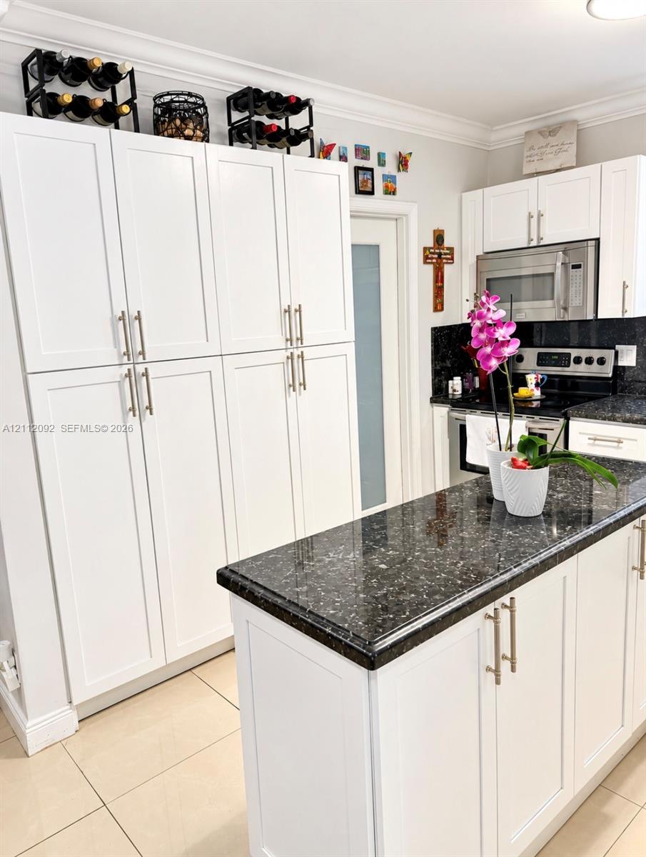 Kitchen featuring white shaker-style cabinetry, a central island with a stone-finish countertop, stainless steel microwave, integrated oven, and tile flooring