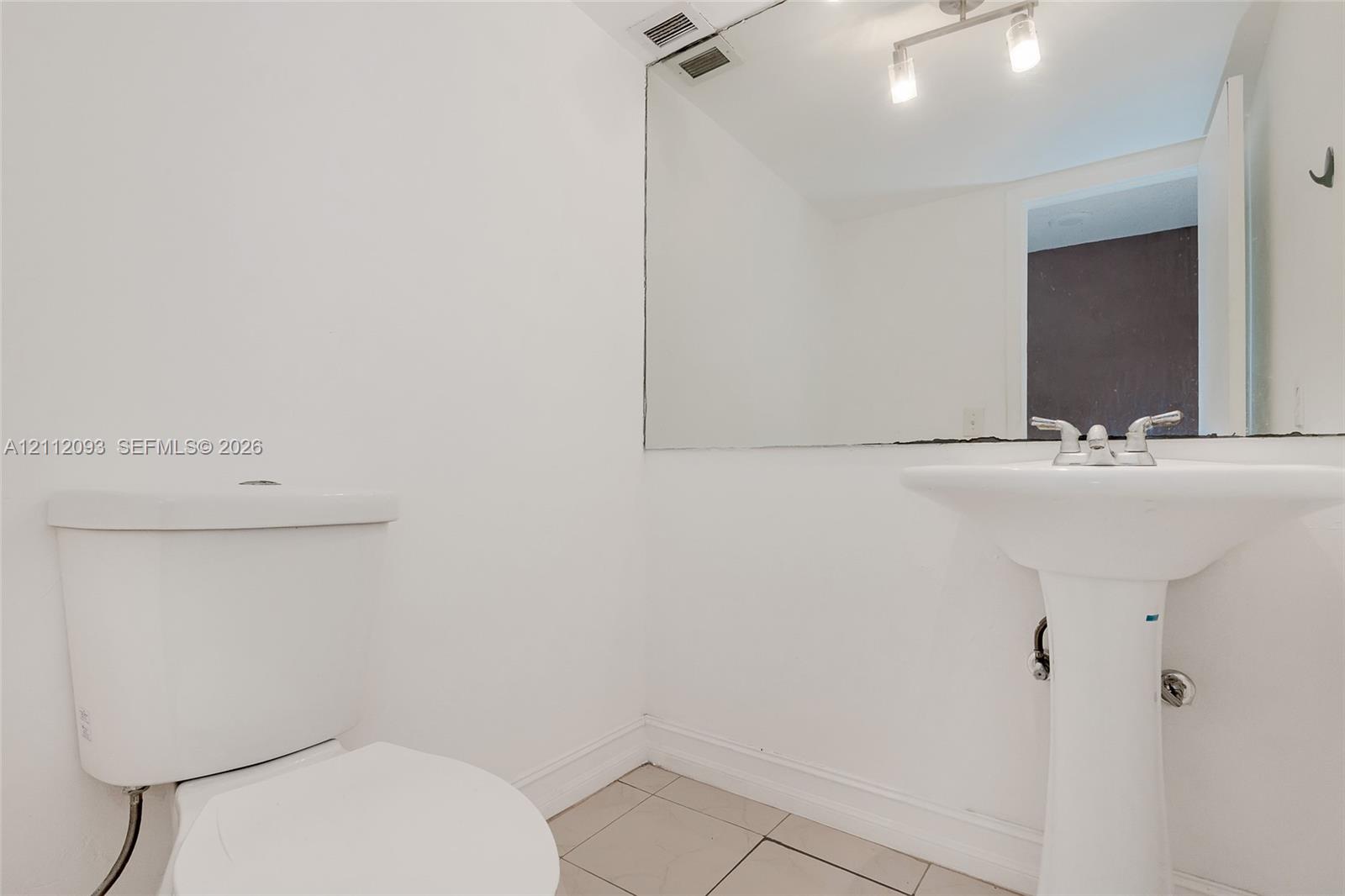 Bathroom featuring a pedestal sink, dual-handle chrome faucet, wall-spanning vanity mirror, multi-light bar fixture, and tile flooring