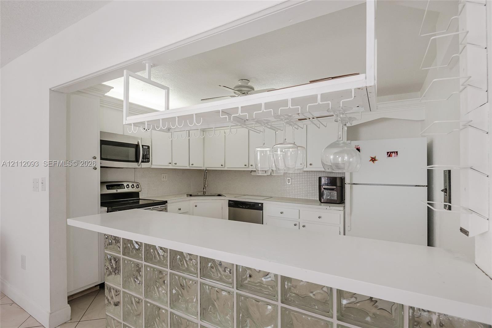 Kitchen featuring white cabinetry, solid-surface breakfast bar, glass block base, and built-in overhead stemware rack Kitchen featuring white cabinetry, solid-surface breakfast bar, glass block base, and built-in overhead stemware rack