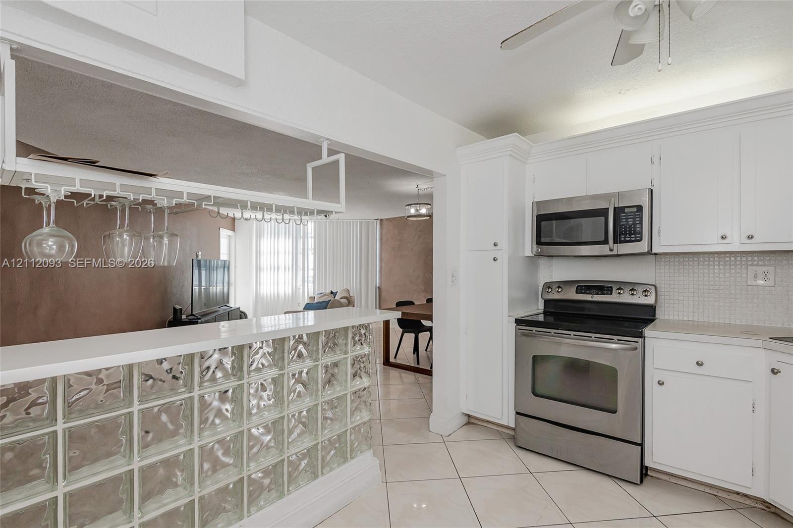 Kitchen featuring white cabinetry, stainless steel appliances, a glass block peninsula, and an overhead stemware rack