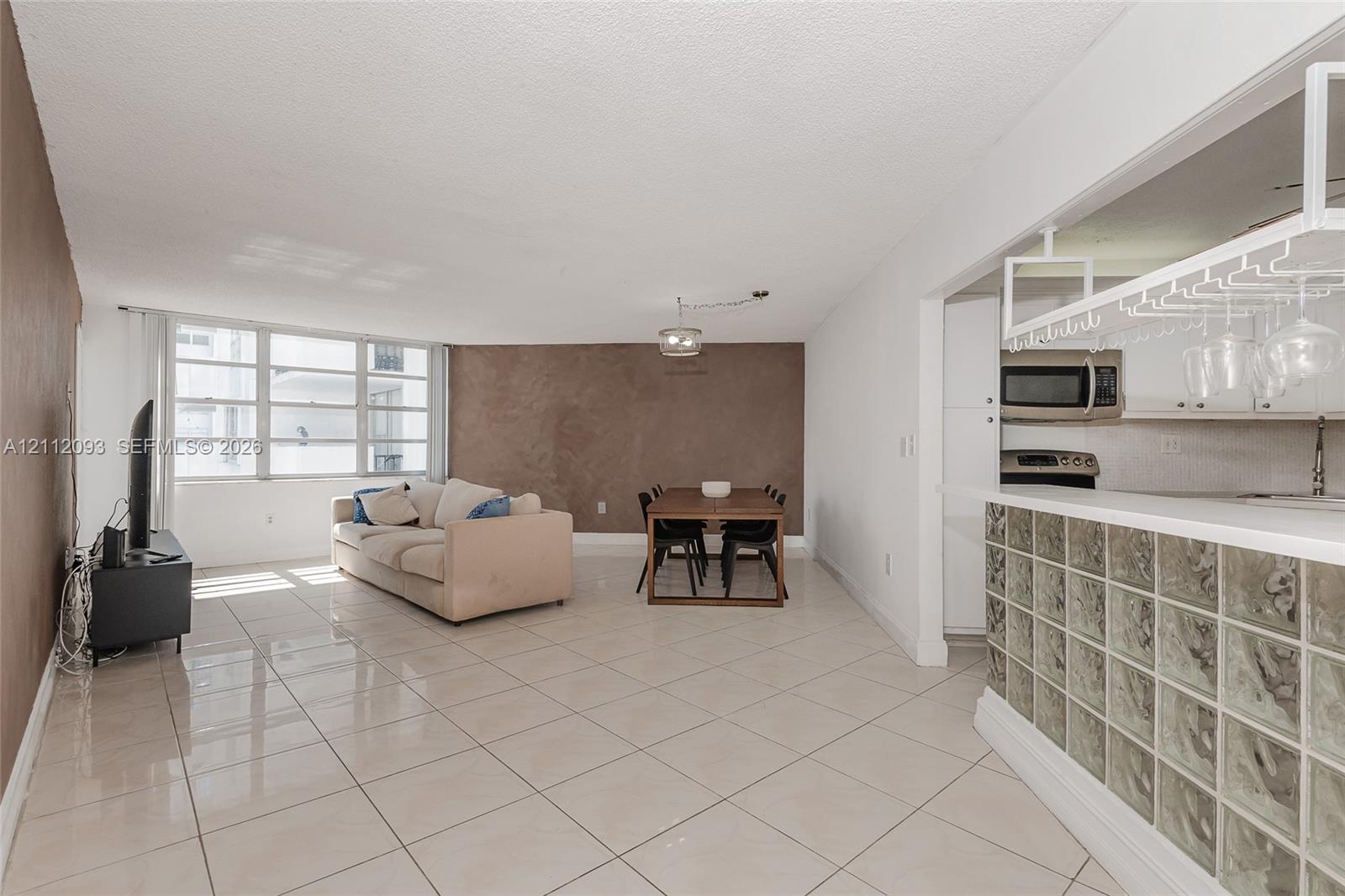 Open-concept interior featuring large-format tile flooring, a glass block breakfast bar, an integrated hanging glass rack, and expansive windows