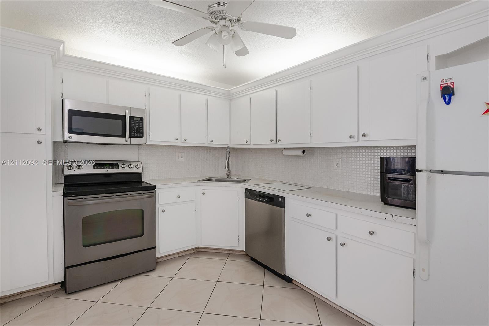 Kitchen featuring white cabinetry with crown molding, stainless steel appliances, tiled backsplash, and ceramic tile flooring