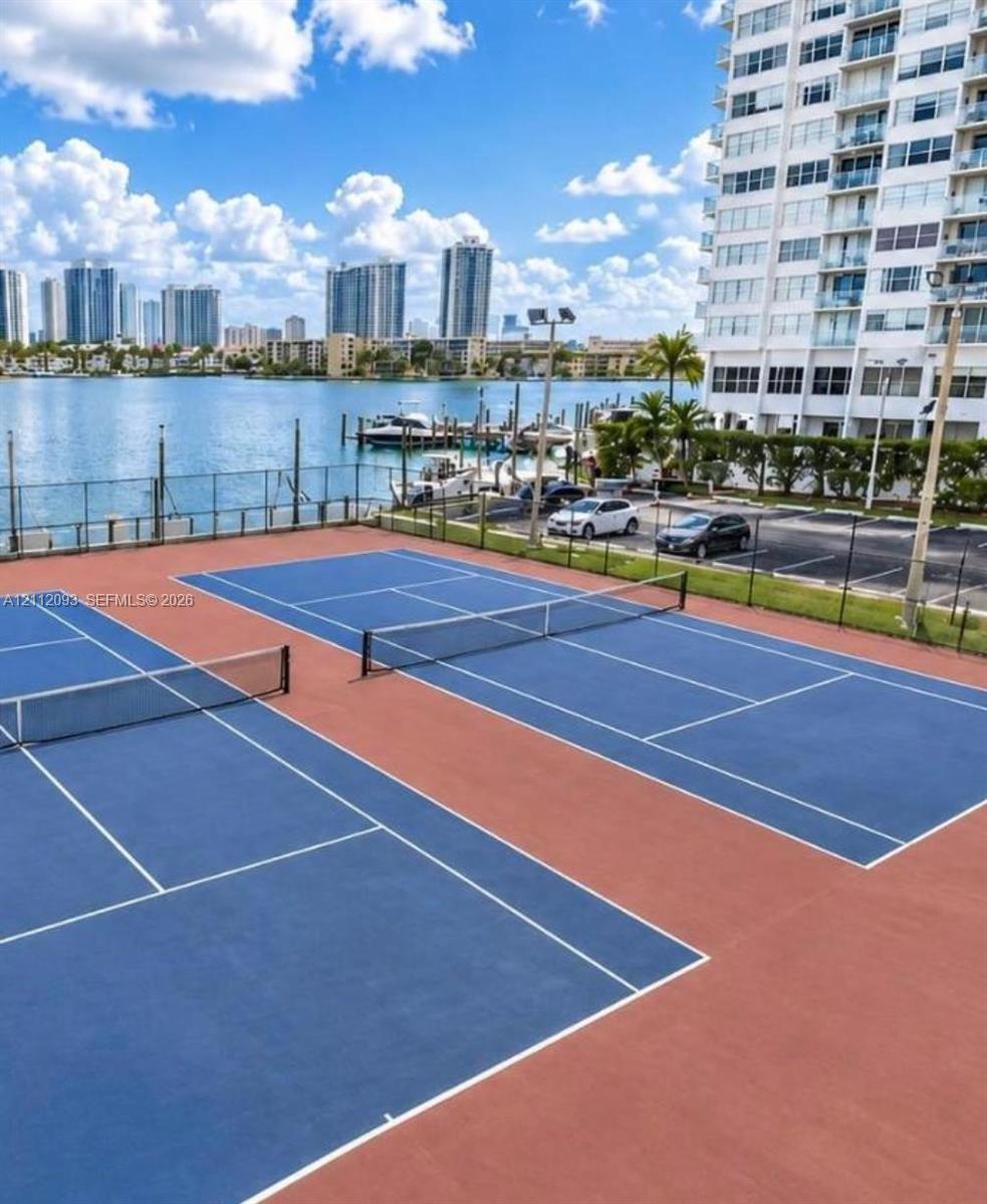 Two hard-surface tennis courts featuring perimeter fencing, metal netting systems, and waterfront positioning