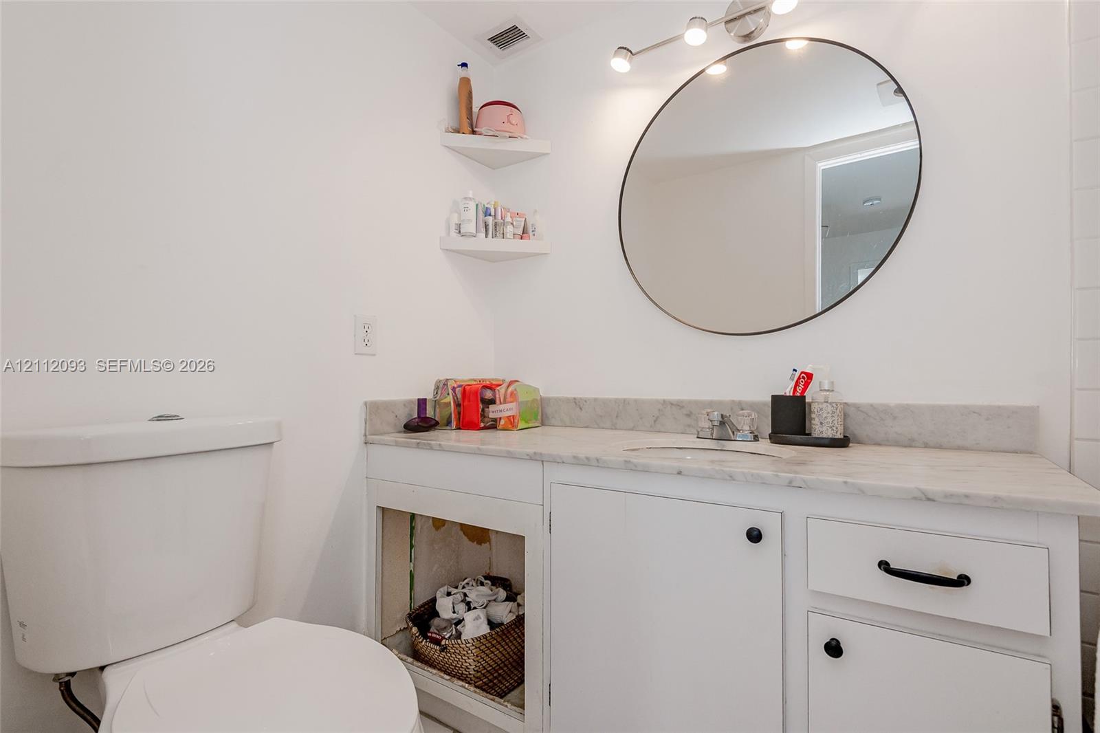 Bathroom featuring a stone vanity countertop with an integrated basin, circular wall-mounted mirror, white shaker-style cabinetry, and multi-bulb track lighting