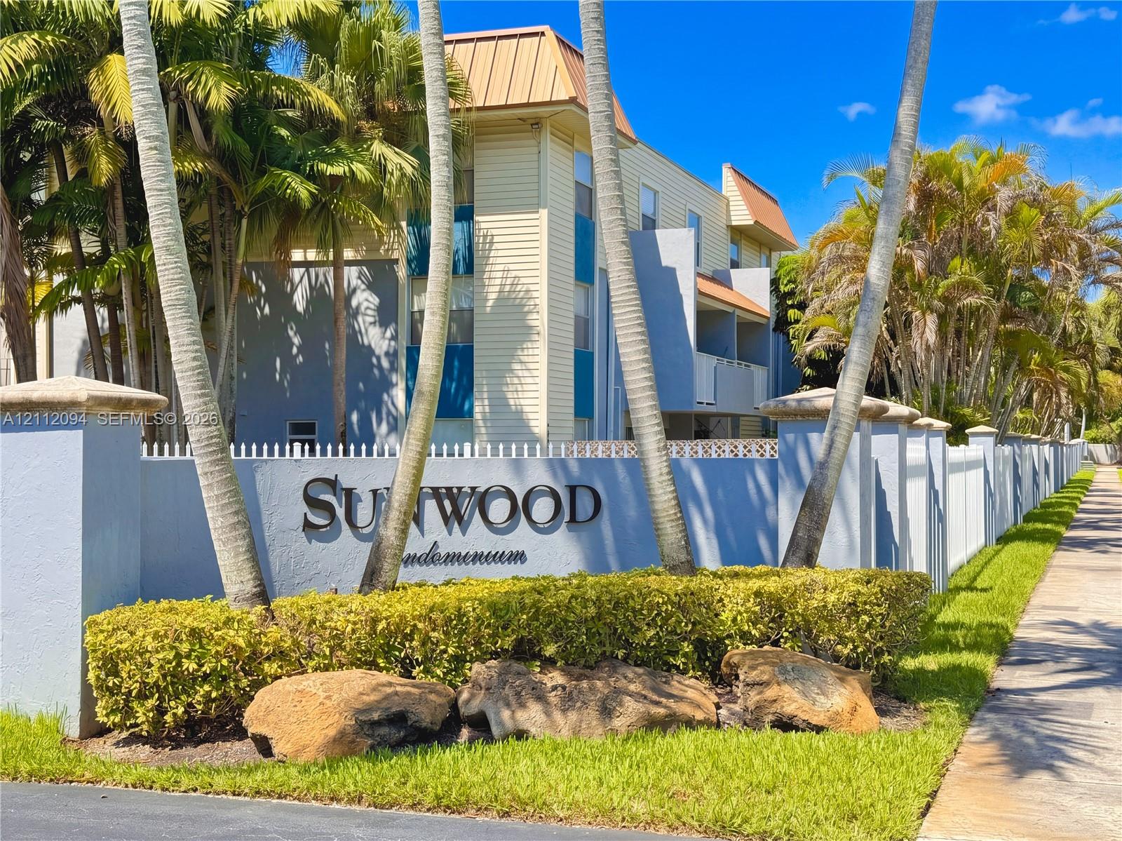 Multi-story building exterior featuring horizontal siding, metal roofing, masonry perimeter wall with integrated signage, and mature palm landscaping Multi-story building exterior featuring horizontal siding, metal roofing, masonry perimeter wall with integrated signage, and mature palm landscaping