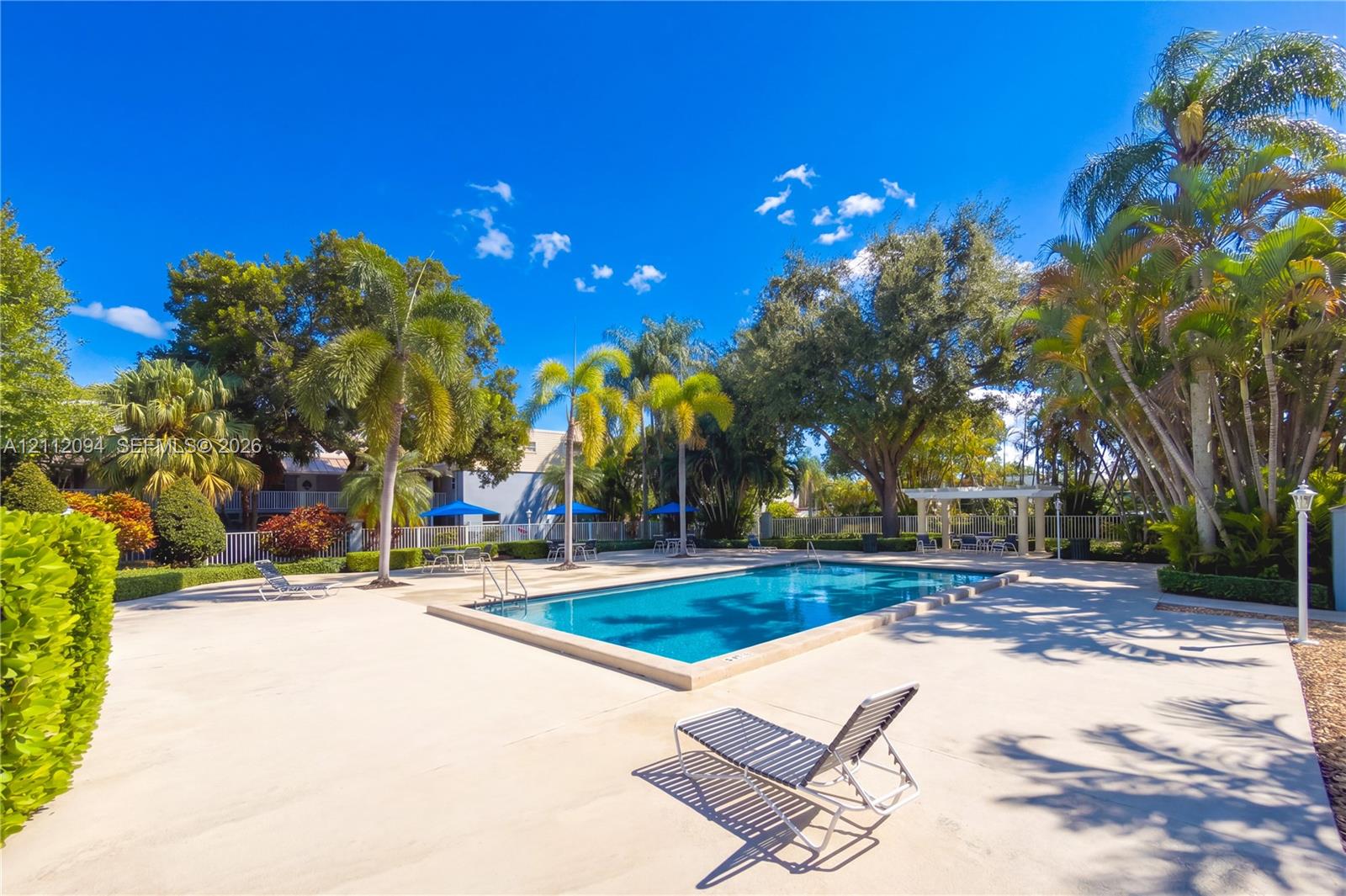 Beautiful community pool and deck area with a pergola, surrounded by lush landscaping