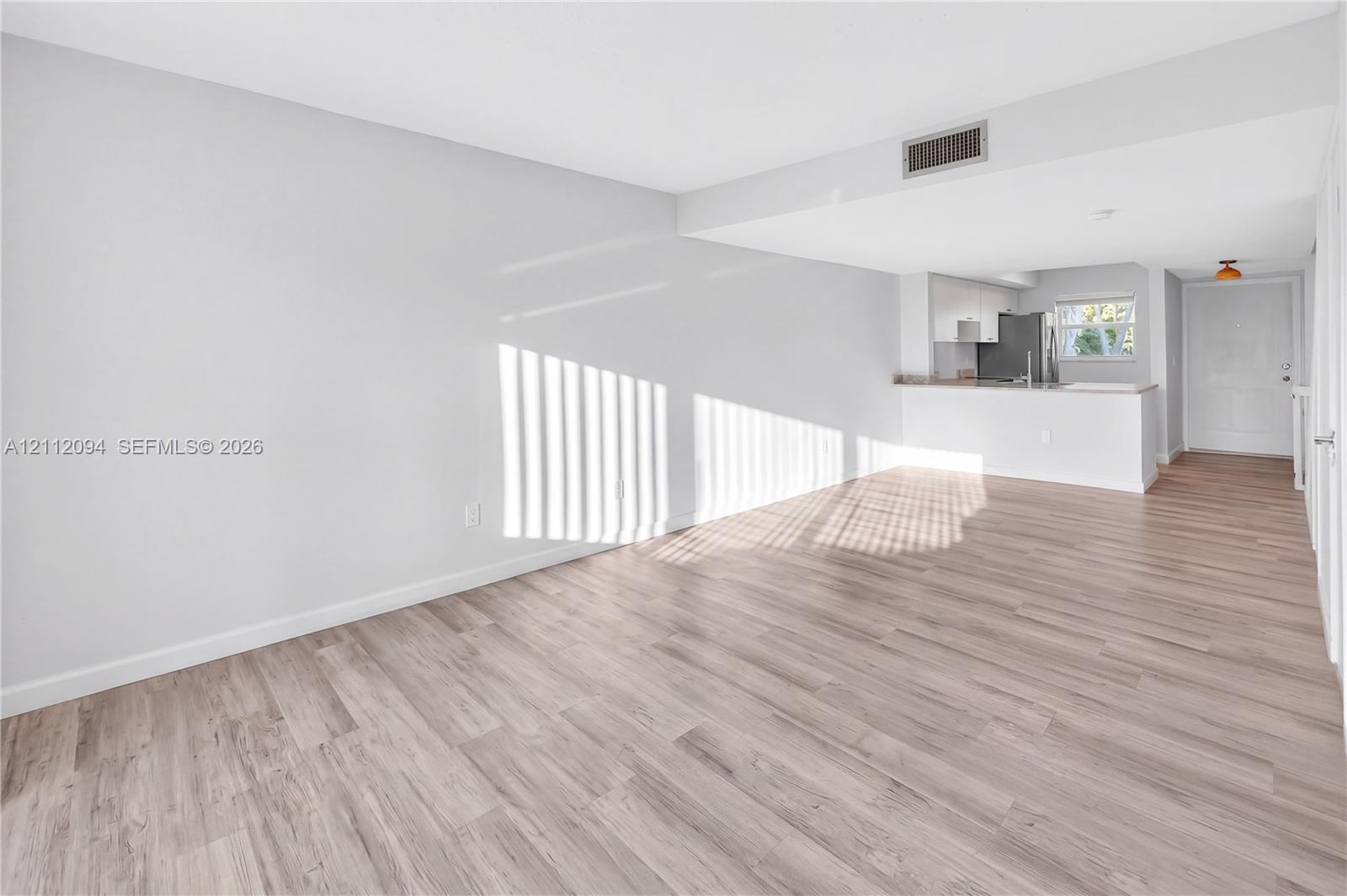 Open-concept interior featuring wood-finish flooring, neutral walls, and a kitchen peninsula with solid-surface countertops Open-concept interior featuring wood-finish flooring, neutral walls, and a kitchen peninsula with solid-surface countertops