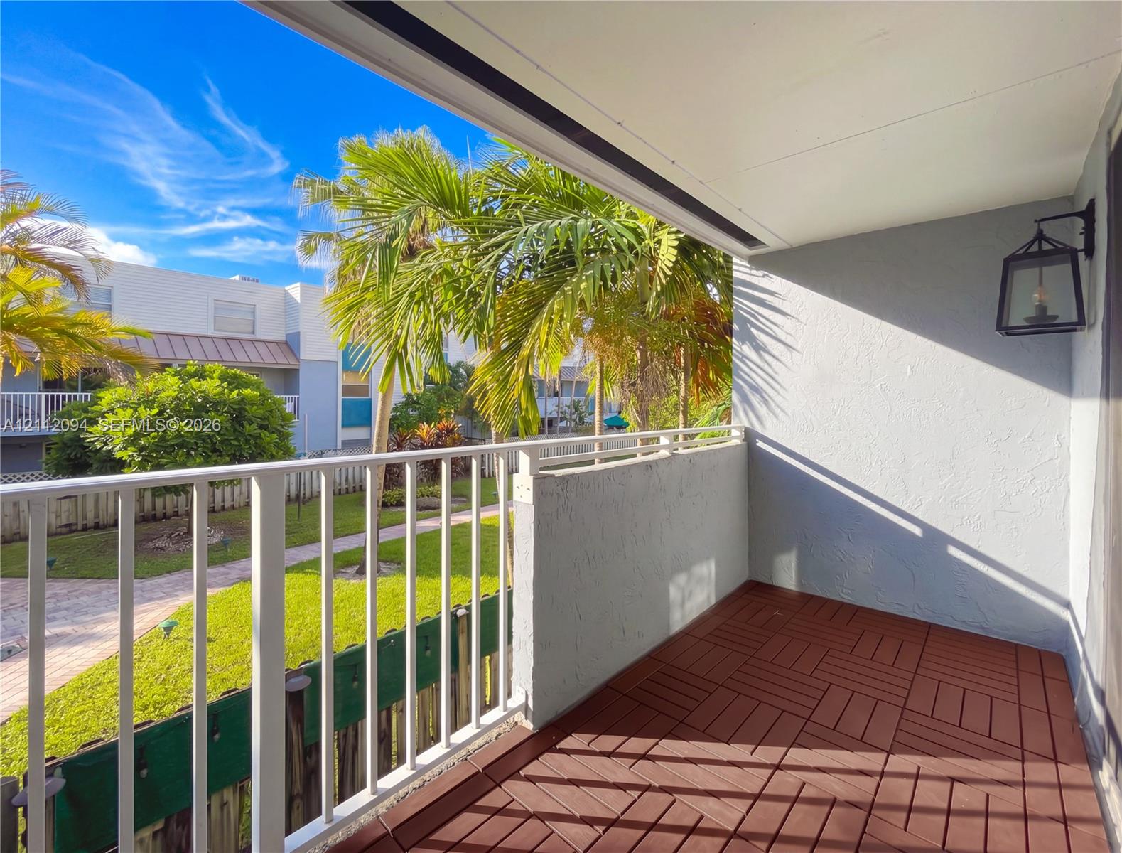 Covered balcony featuring wood-finish deck tiling, a white metal railing, and a black exterior wall-mounted lantern