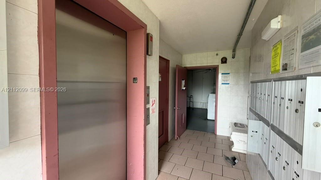 Stainless steel elevator with a pink-toned frame, tiled flooring, and a wall-mounted bank of secure metal mailboxes
