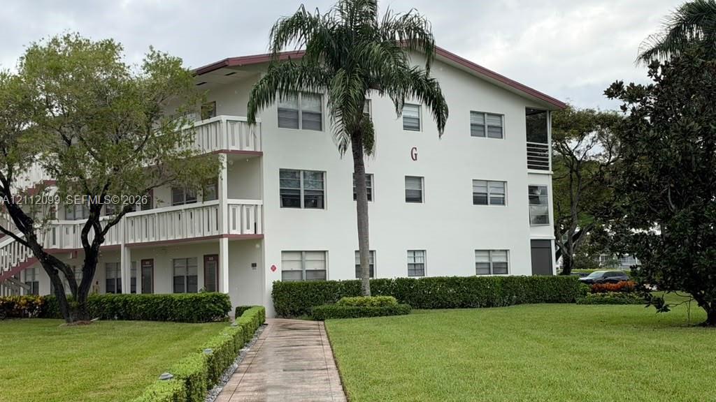 Multi-level exterior with white stucco facade, stacked balconies, tiled walkway, and mature landscaping