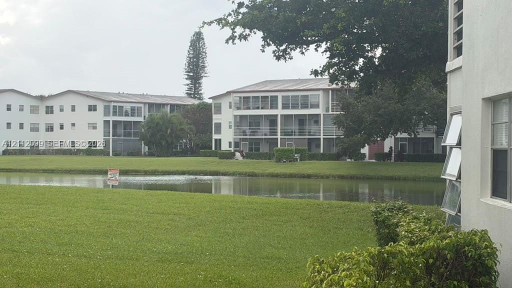 Multi-story residential buildings featuring screened-in lanais, light-toned exterior finish, expansive common area lawn, and pond frontage