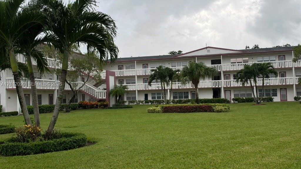 Multi-story exterior featuring white balustrade balconies, expansive manicured lawn, and mature palm trees